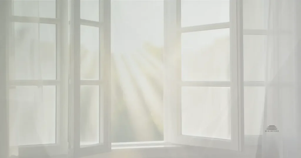 Open window with sheer curtains and soft sunlight filtering into a bright room.