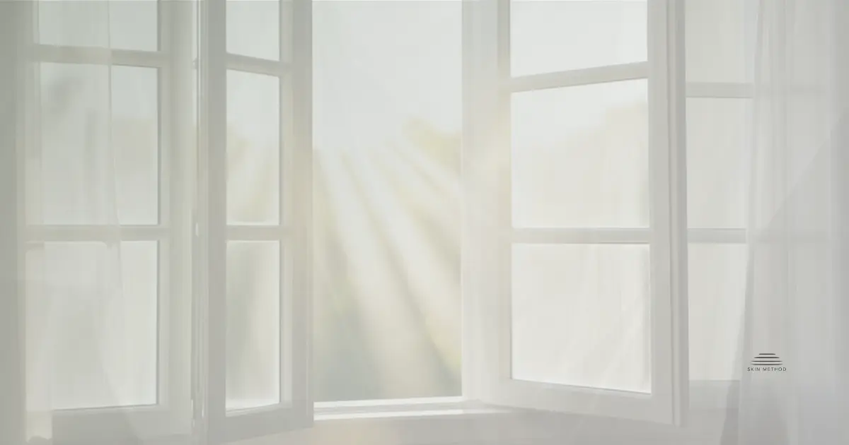 Open window with sheer curtains and soft sunlight filtering into a bright room.
