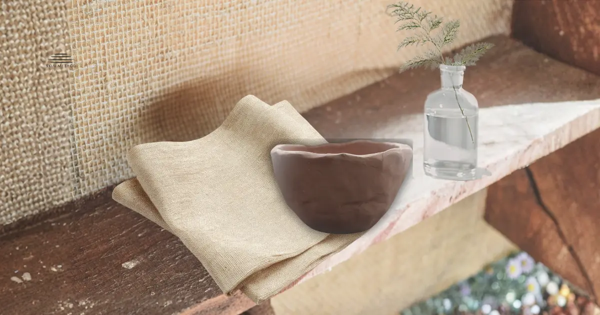 Folded linen, a ceramic vessel, and a glass bottle arranged together on a wooden shelf in natural light.