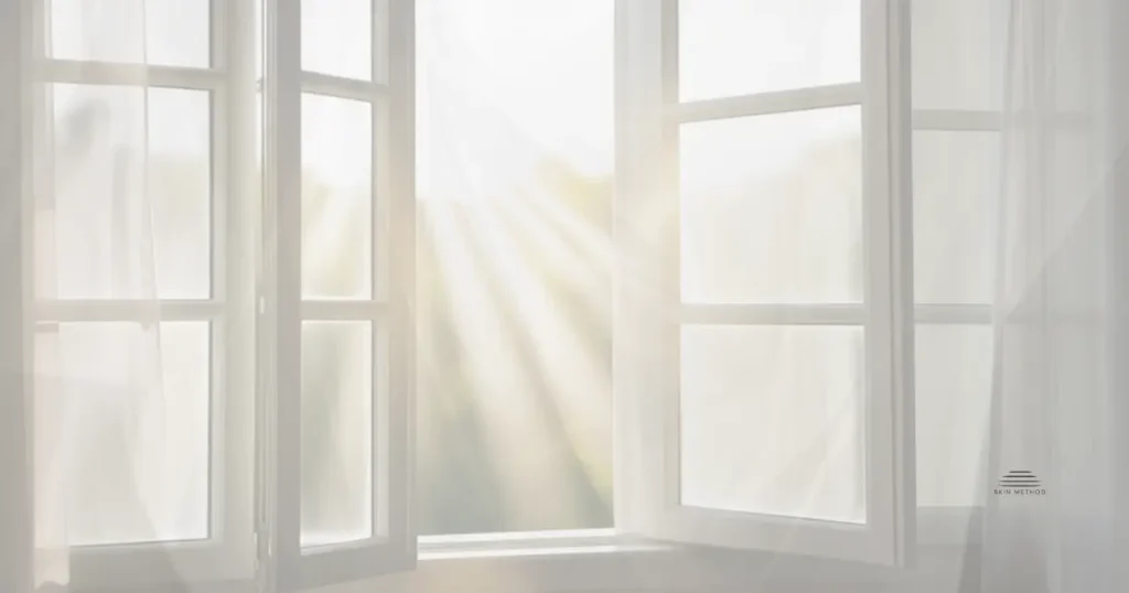 Open window with sheer curtains and soft sunlight filtering into a bright room.