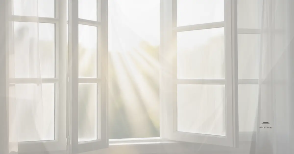 Open window with sheer curtains and soft sunlight filtering into a bright room.