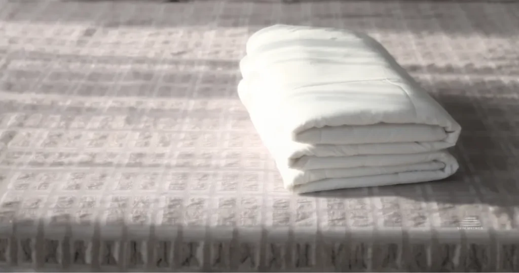 Folded white linen resting on a textured fabric surface in soft natural light.