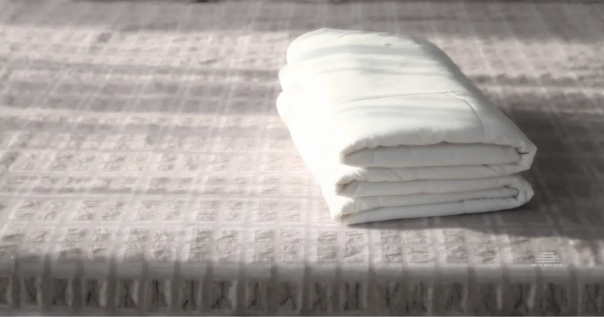 Folded white linen resting on a textured fabric surface in soft natural light.