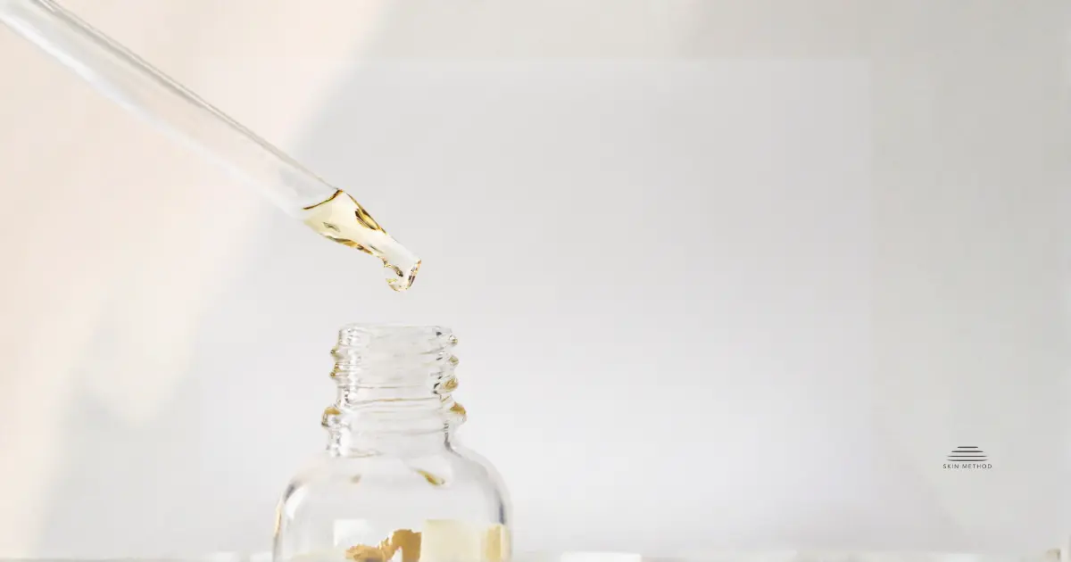 A glass dropper with pale serum suspended above an open, unbranded skincare bottle on a light neutral background.